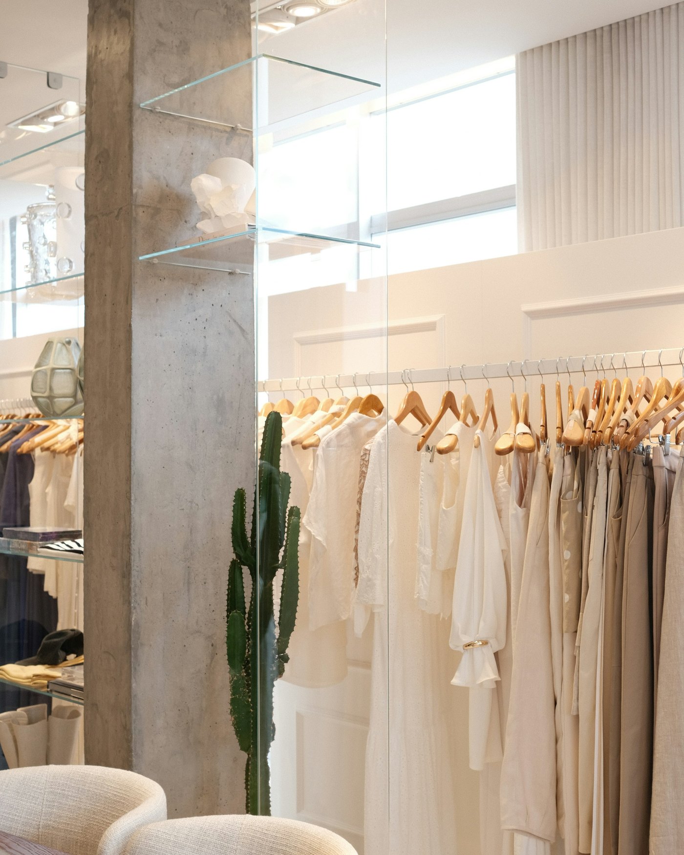 Boutique luminosa e minimale, capi color crema appesi in fila e un cactus